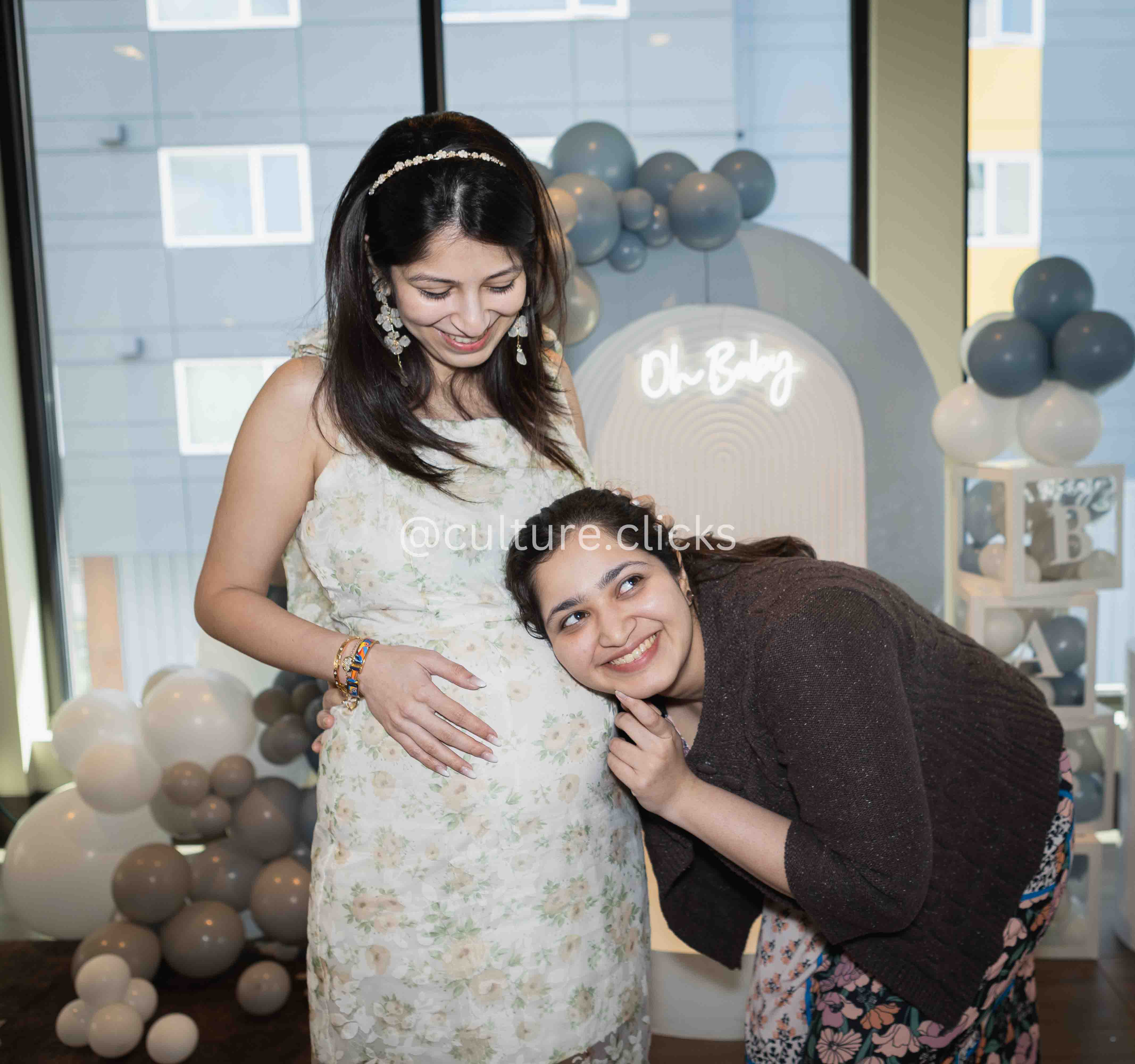 Baby shower photography of a pregnanat mom with sister. hugging and listening to baby, captured by cultureclicks photography with decorations done by cultureclicks